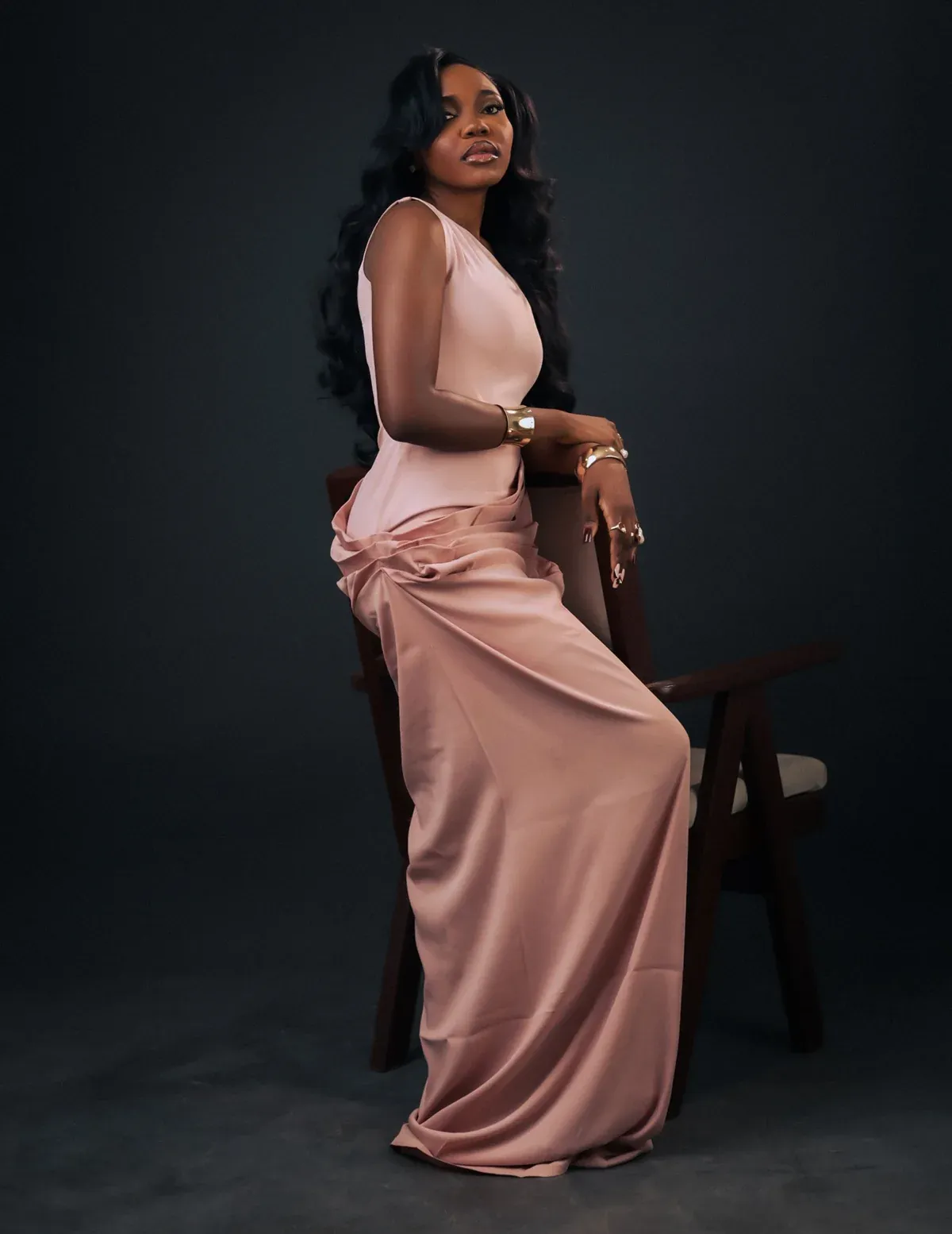 Modelo sentada com vestido longo rosa-velho de cetim e saia drapeada